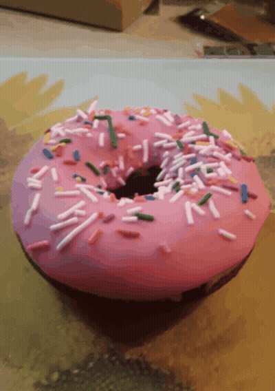 A Pink Donut With Sprinkles And A Hole In It GIF
