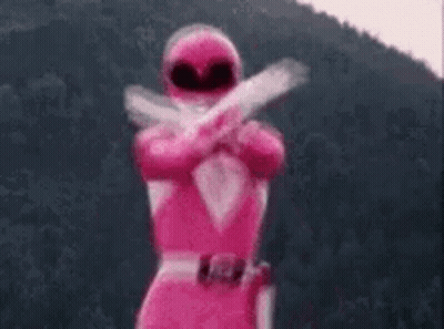 A Pink Power Ranger Is Standing In Front Of A Mountain Holding Two Guns . GIF