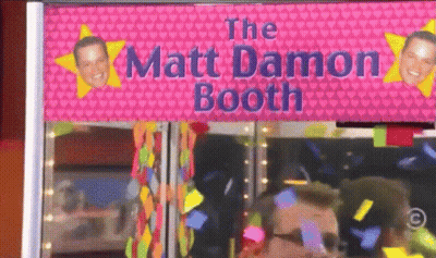 A Pink Sign That Says The Matt Damon Booth Is Above A Man GIF