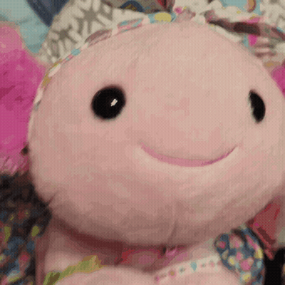 A Pink Stuffed Animal With Black Eyes And A Smile On Its Face GIF