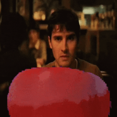 A Pixelated Image Of A Man Sitting In Front Of A Red Object GIF