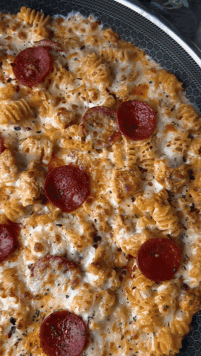 A Pizza With Pepperoni And Macaroni And Cheese In A Pan GIF
