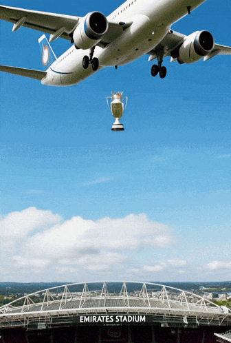A Plane Is Flying Over Emirates Stadium With A Trophy Hanging From The Wing GIF