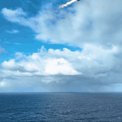 A Plane Is Flying Over The Ocean With A Blue Sky And White Clouds GIF
