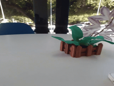 A Plant In A Small Wooden Planter Sits On A White Table GIF