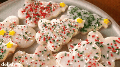 A Plate Of Christmas Cookies With Icing And Sprinkles And The Word Delish On The Bottom GIF