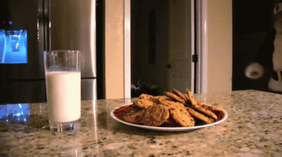 A Plate Of Cookies Next To A Glass Of Milk On A Counter GIF