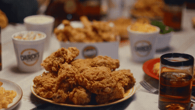 A Plate Of Fried Chicken Sits On A Table Next To A Cup That Says Bourbon 'S GIF