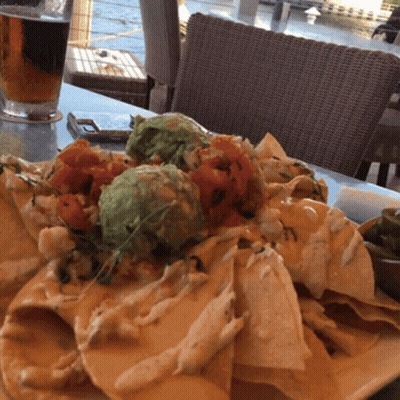 A Plate Of Nachos Sits On A Table With A Glass Of Beer In The Background GIF