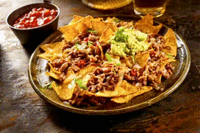 A Plate Of Nachos With Guacamole And Salsa Next To A Bowl Of Salsa On A Table . GIF
