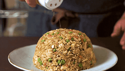 A Plate Of Rice And Vegetables With A Person Pouring Salt On Top GIF