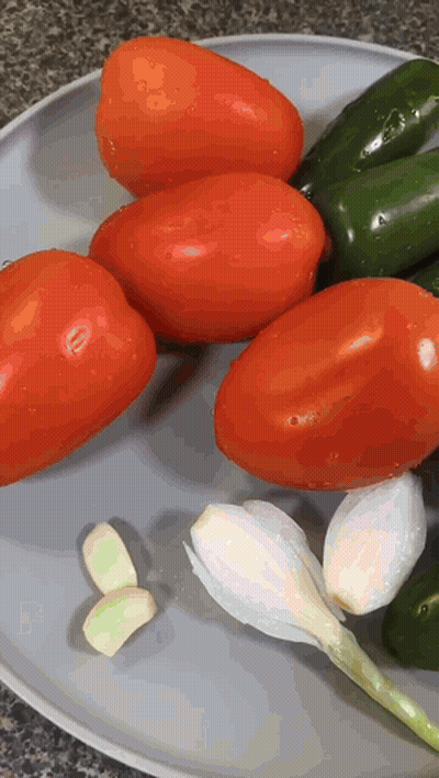 A Plate Of Tomatoes Peppers And Garlic On A Counter Top GIF