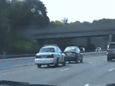 A Police Car Is Driving Down A Highway Next To A Black Car . GIF