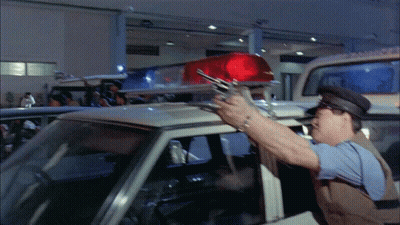 A Police Officer Holds A Gun In Front Of A Police Car GIF
