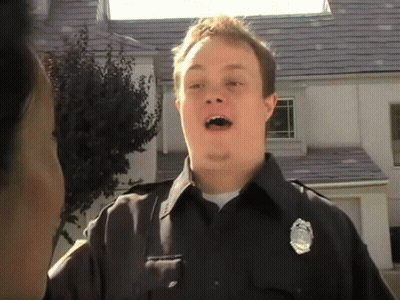 A Police Officer In Front Of A House With A Badge On His Chest GIF