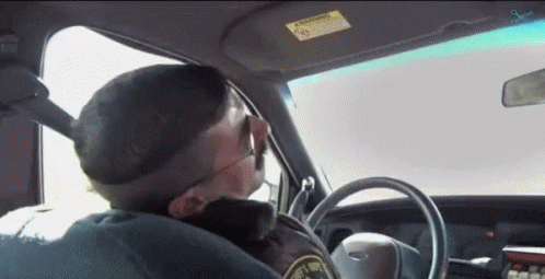 A Police Officer Is Driving A Car And Smoking A Cigarette While Wearing Sunglasses . GIF