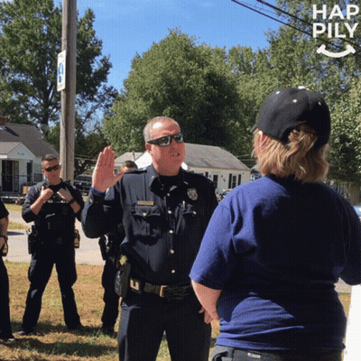 A Police Officer Is Giving A Speech To A Woman In Front Of A Sign That Says Hap Pily GIF