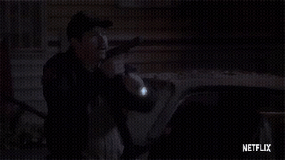 A Police Officer Is Holding A Gun In Front Of A Car At Night . GIF