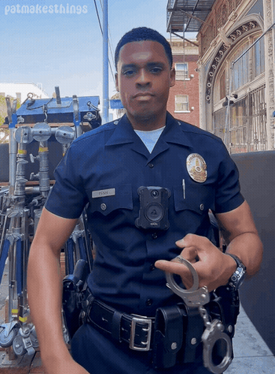 A Police Officer Is Holding A Pair Of Handcuffs In Front Of A Building With Patmakesthings Written Below Him GIF