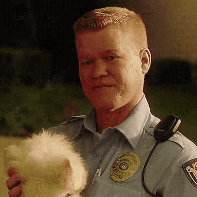 A Police Officer Is Holding A Small White Dog In His Arms GIF