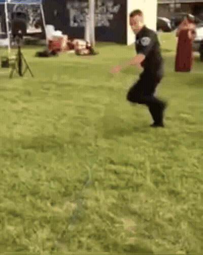 A Police Officer Is Jumping In The Grass . GIF