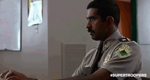A Police Officer Is Sitting At A Desk In Front Of A Computer . GIF