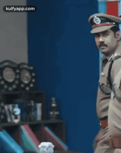 A Police Officer Is Standing In A Room With A Lot Of Trophies On The Shelf . GIF