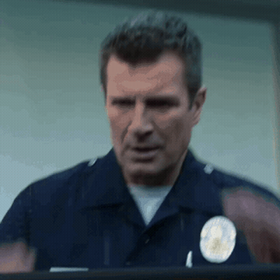 A Police Officer Is Standing In Front Of A Window And Looking Out . GIF