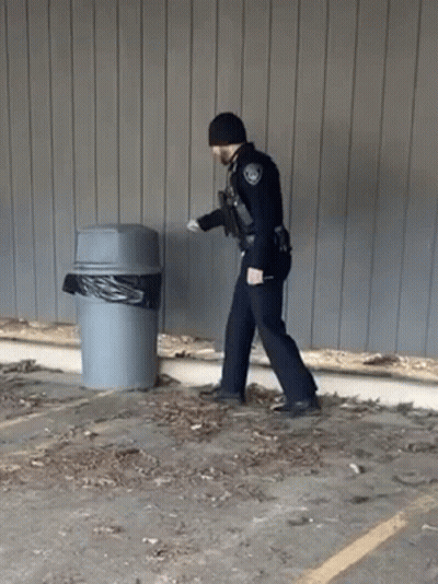 A Police Officer Is Walking Towards A Trash Can . GIF