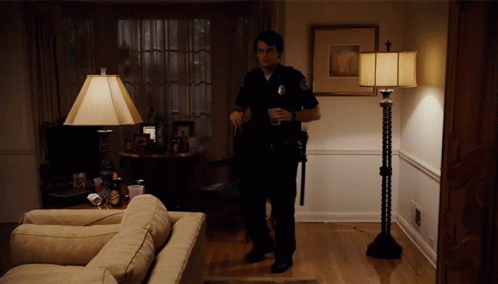 A Police Officer Stands In A Living Room Holding A Cup GIF