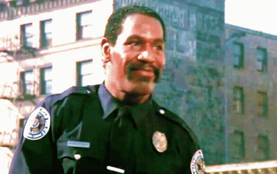 A Police Officer Stands In Front Of A Building With The Letter F On The Side GIF