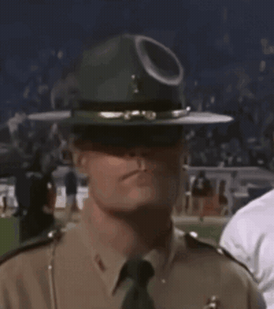 A Police Officer Wearing A Hat And Sunglasses Is Standing In A Crowd . GIF