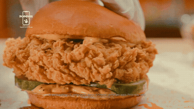 A Popeye 'S Chicken Sandwich With A Pickle On Top GIF