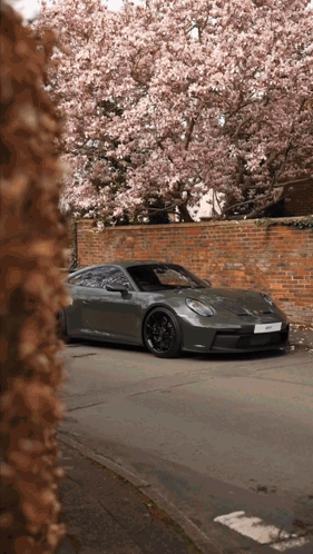 A Porsche Sports Car Is Parked In Front Of A Brick Wall GIF