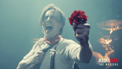 A Poster For Hadestown The Musical Shows A Man Holding A Red Flower In His Hand GIF