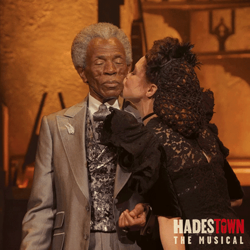 A Poster For Hadestown The Musical Shows A Woman Kissing An Old Man On The Cheek GIF