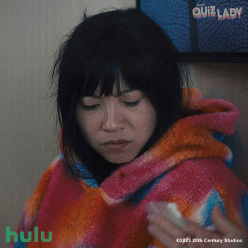A Poster For Quiz Lady Shows A Woman In A Pink And Orange Blanket GIF
