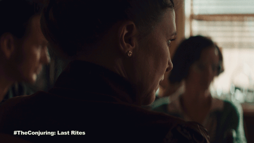 A Poster For The Conjuring Last Rites Shows A Woman Sitting At A Table GIF