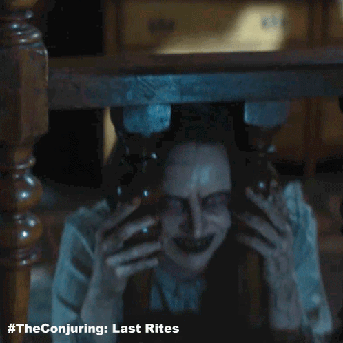 A Poster For The Conjuring Last Rites With A Scary Woman Behind A Table GIF