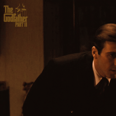 A Poster For The Godfather Part Ii Shows A Man In A Suit And Tie Sitting On A Couch GIF