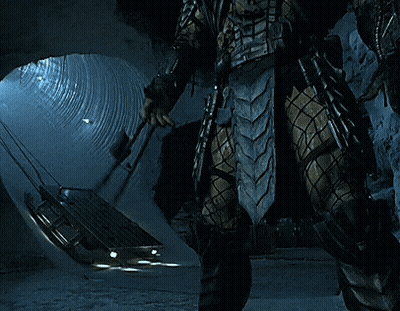 A Predator Is Standing In A Tunnel Holding A Spear GIF