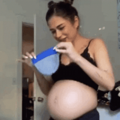 A Pregnant Woman In A Black Top Is Holding A Blue Bowl . GIF