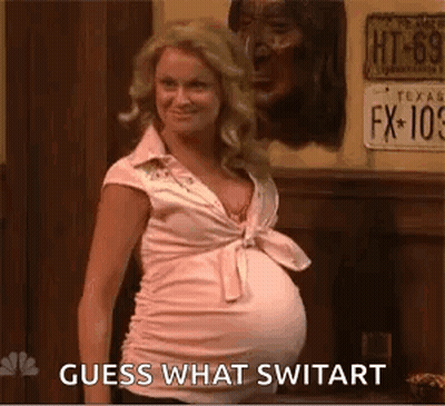 A Pregnant Woman In A Pink Shirt Is Standing In Front Of A Sign That Says Guess What Switart . GIF