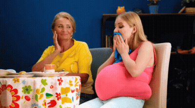 A Pregnant Woman Is Sitting At A Table With A Floral Tablecloth GIF