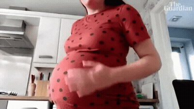 A Pregnant Woman Is Standing In A Kitchen Holding Her Belly . GIF