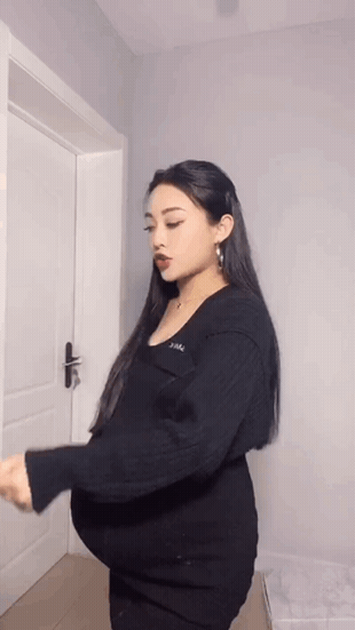 A Pregnant Woman Is Standing In Front Of A Door Holding Her Belly . GIF