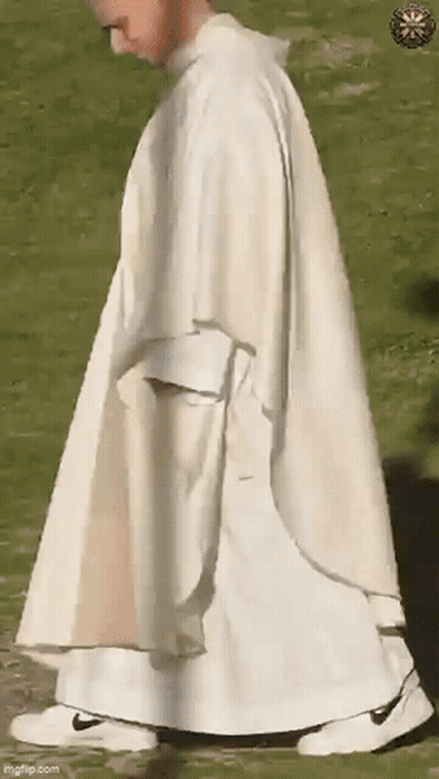 A Priest In A White Robe And White Sneakers Is Walking In A Field . GIF