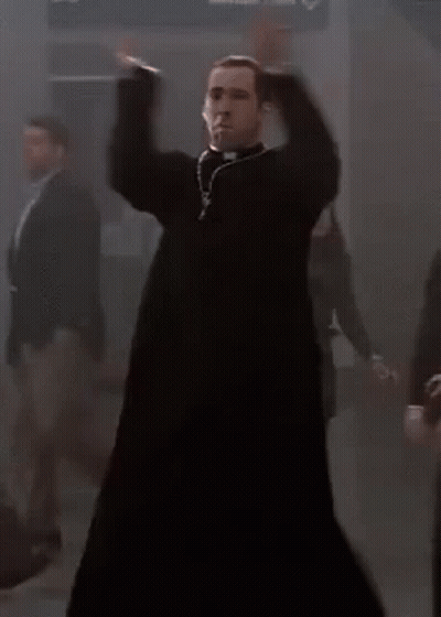A Priest Is Dancing In A Dark Room With A Group Of People Behind Him . GIF