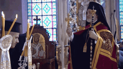 A Priest Is Holding A Cross In Front Of A Stained Glass Window In A Church GIF
