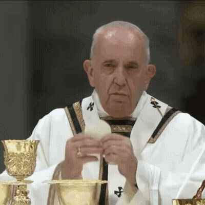A Priest Is Holding A Piece Of Bread In Front Of A Chalice GIF